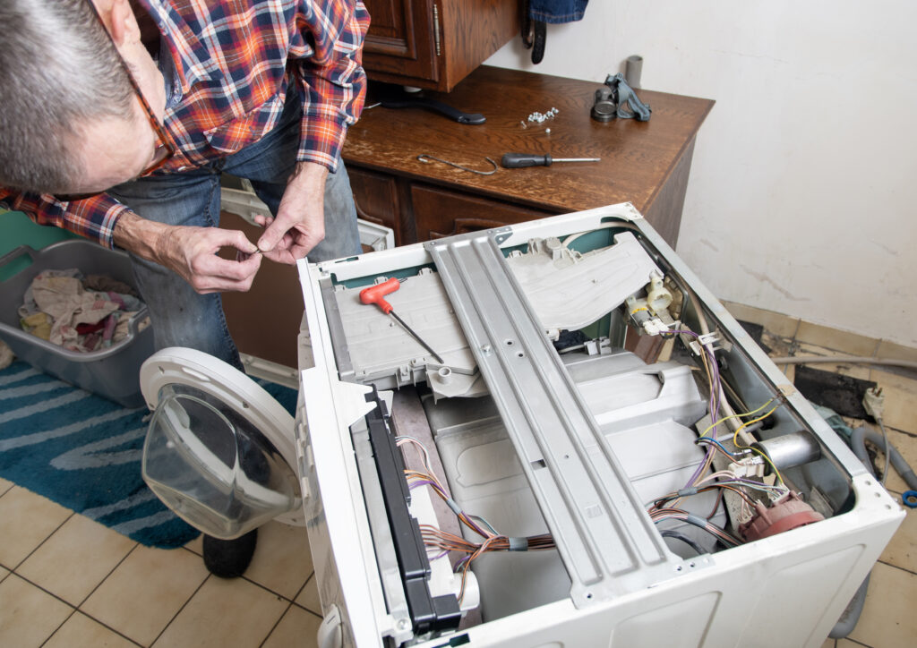 middle aged master in checkered suit unscrews the lid of washing machine with screwdriver for repair